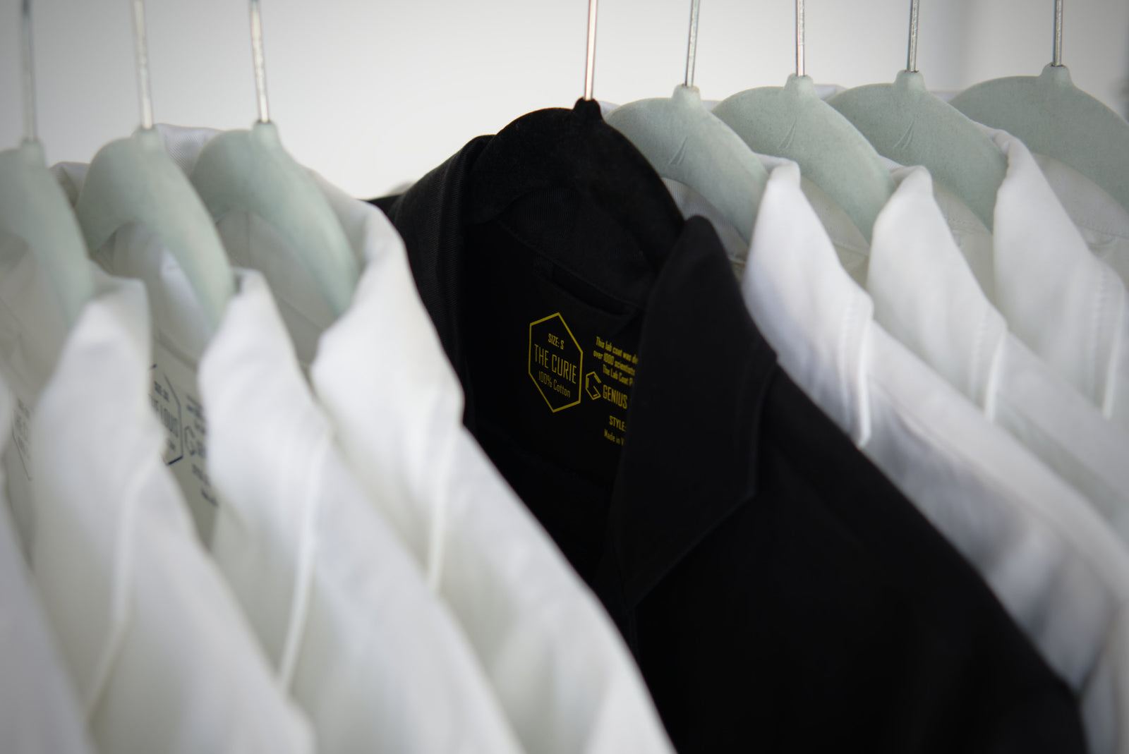 black and white cotton lab coats from genius lab gear on hangers on a rack in a chemistry laboratory