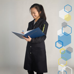 skinny short woman wearing a fitted long knee length black chemistry lab coat holding a science laboratory notebook and writing in it with a pen while holding utensils and markers in her pockets