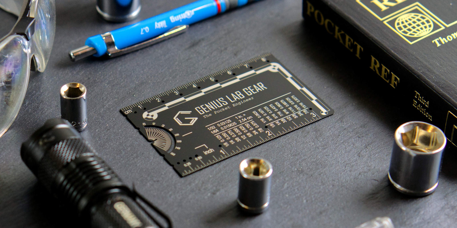 Genius Lab Gear Pocket Tool gift for engineers called The Pocket Engineer on work bench next to wrenches, safety glasses, bolts, nuts, and a pocket reference