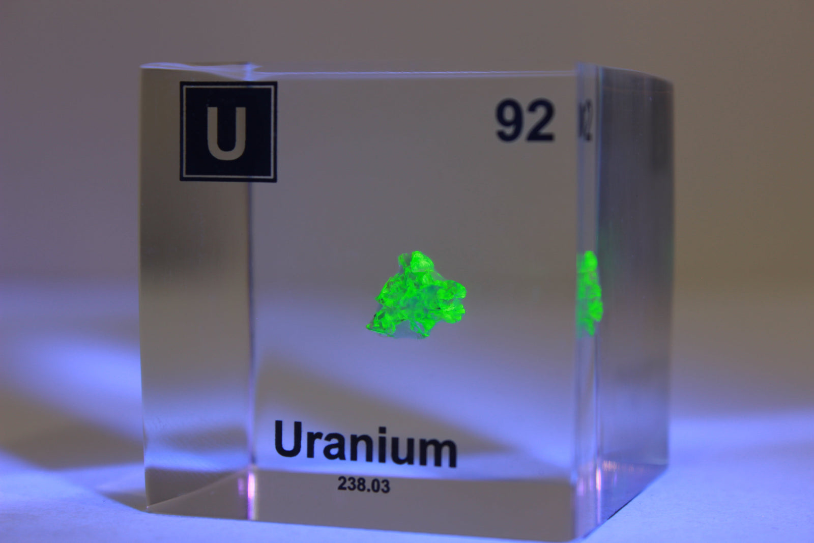 Uranium element cube glowing green under UV light on white background, collector gift