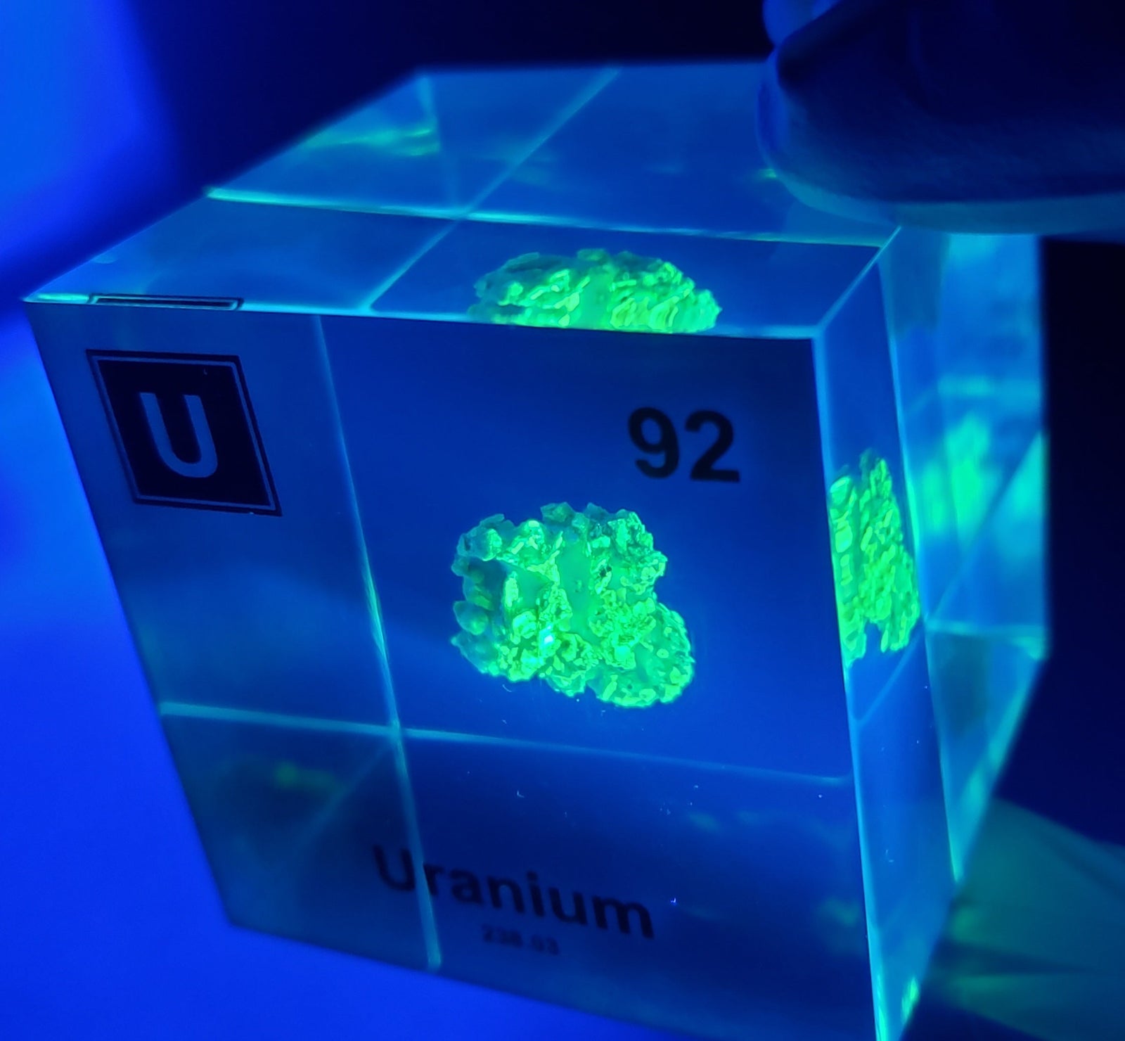 Uranium element cube glowing green under UV light held in hand, unique collector gift