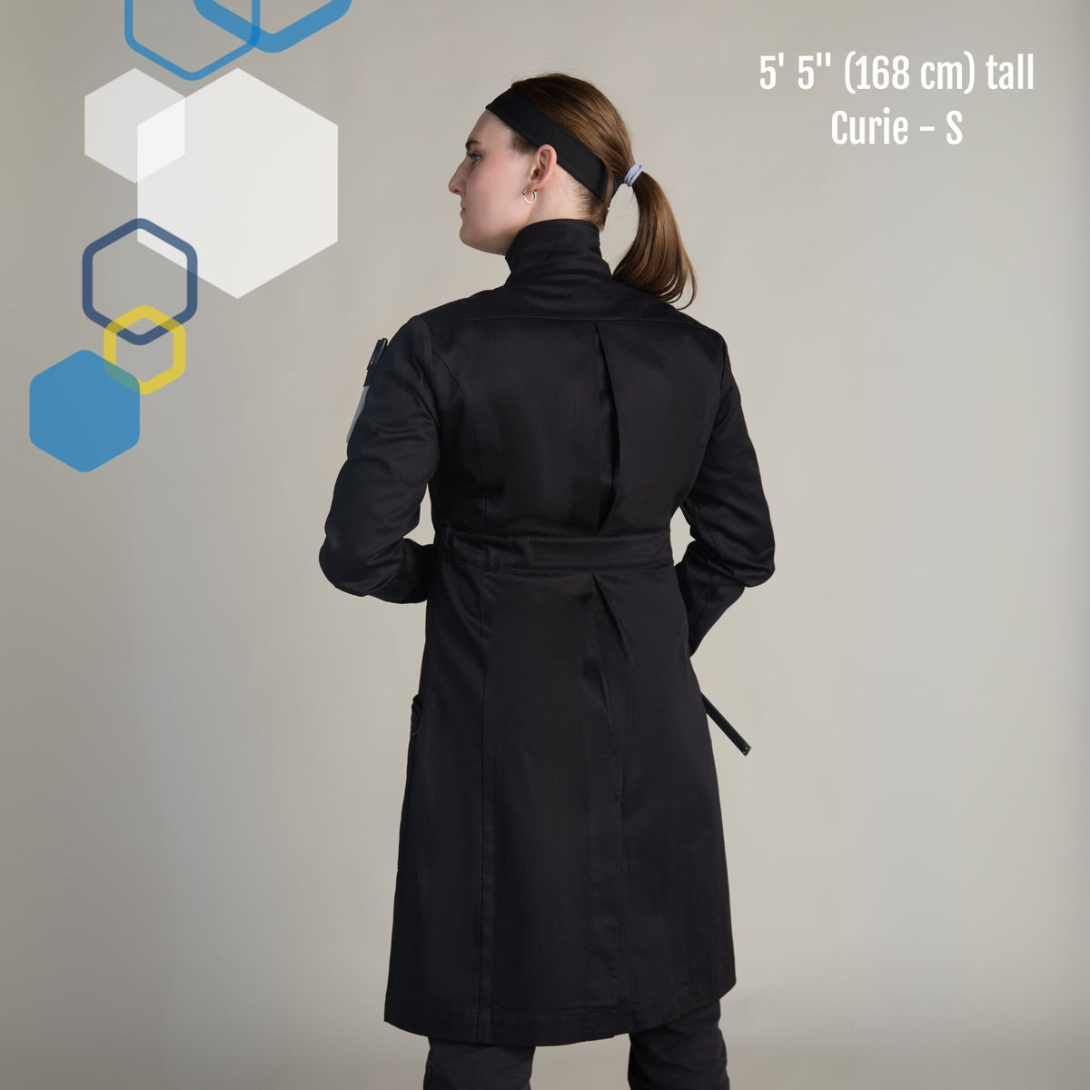 female chemist wearing a fitted black cotton lab coat with adjustable waist belt and princess cut. Showing high collar howie style for extra protection. Curie lab coat from genius lab gear