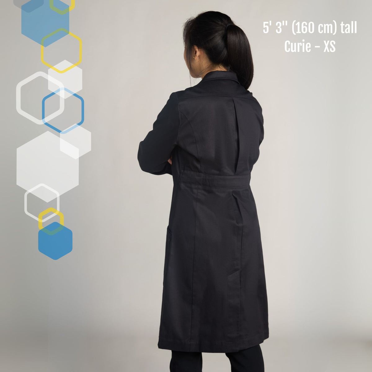 petite short small college student woman wearing a cool chemistry lab coat with expandable back pleat and adjustable belt to tighten the waist. Facing away with arms crossed. 
