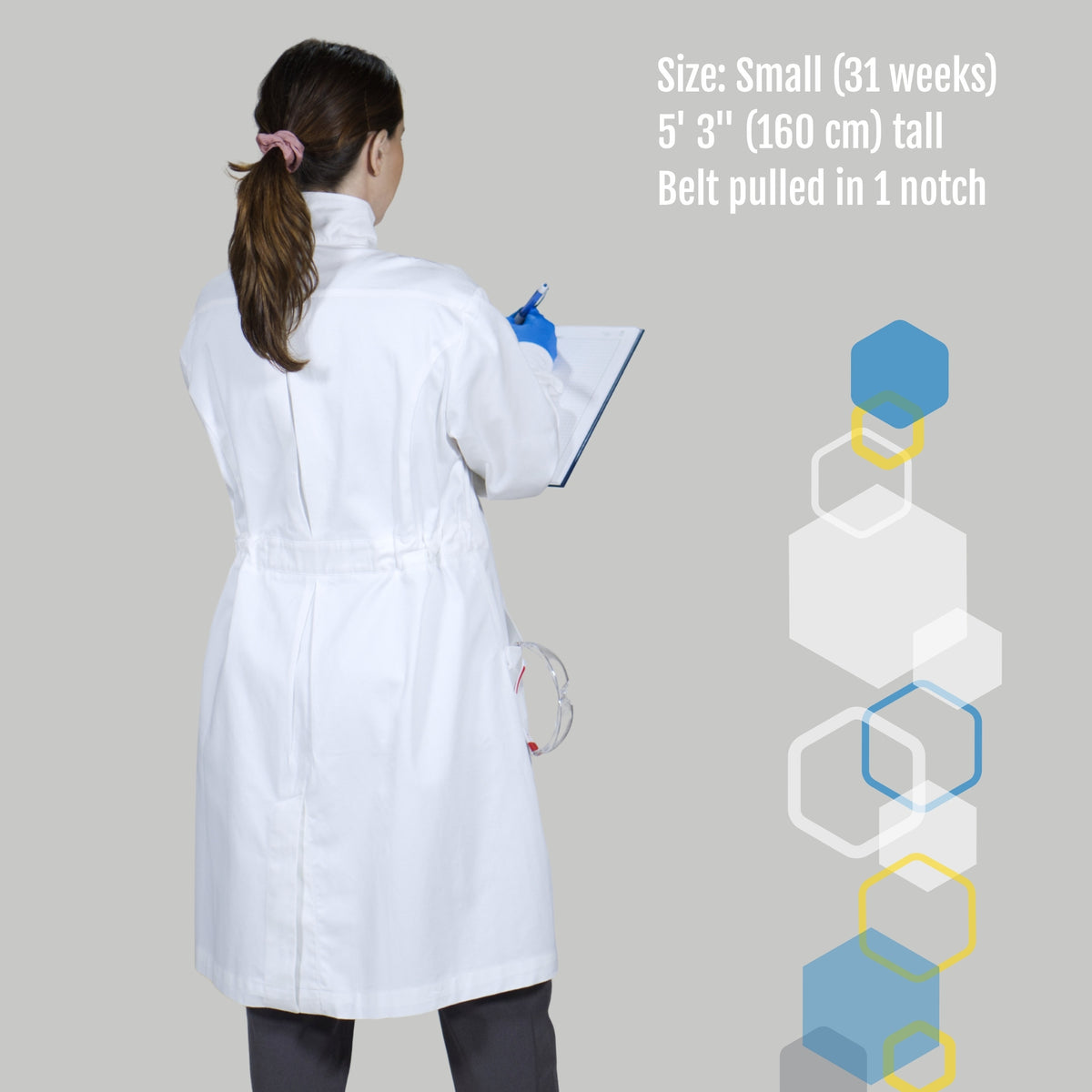 the Alma lab coat for pregnant scientists doing research - woman writing in laboratory notebook after experiment with safety glasses hanging and rear pleats showing for expansion