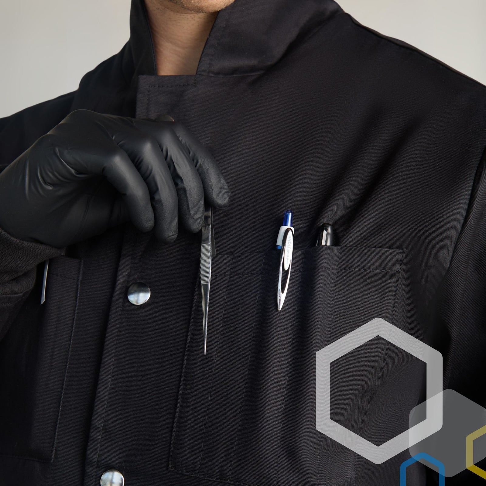 male scientist using tweezers and putting pens and markers into the upper breast pocket individual tool slots on a black lab coat for biology wearing black gloves by genius lab gear