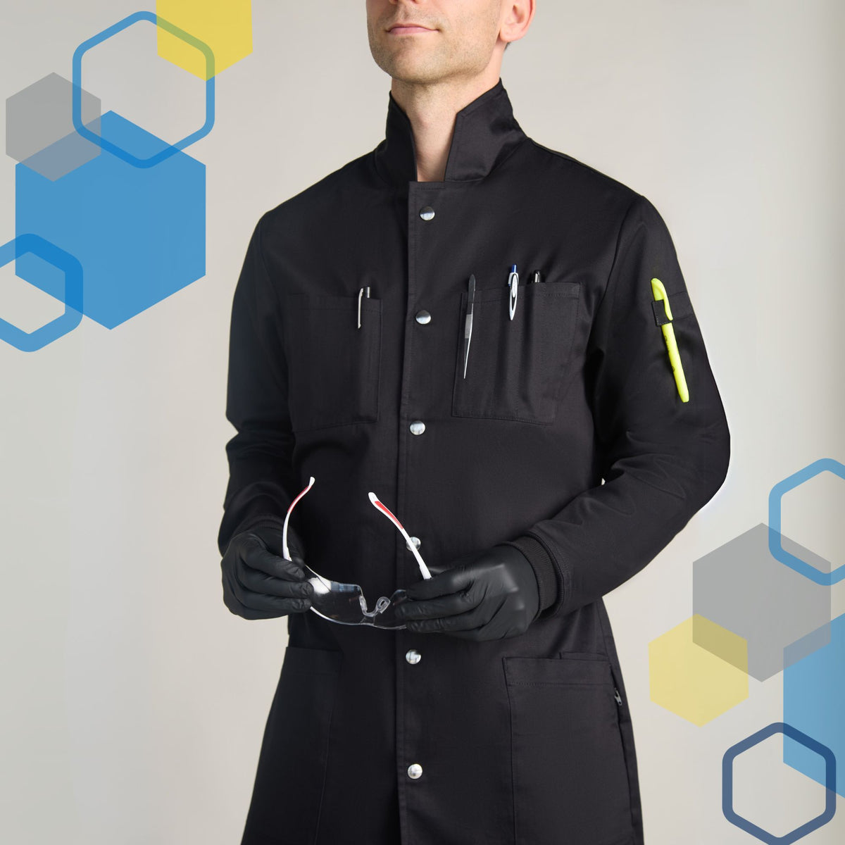 men's full length scientist lab coat with howie style tall collar, metal snap front closure for extra safety, and 6 pockets for utensil storage. Holding safety glasses and wearing black nitrile gloves for chemistry laboratory classes.