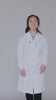 Petite woman wearing the XS black Curie lab coat showing pockets, zippers, snaps, knit cuffs, and adjustable belt