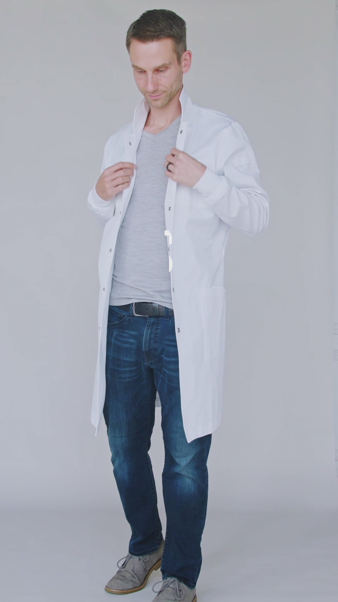 men's black cotton lab coat feature video showing 6 ft tall male using pen pockets, zippers, snaps, stretching and adjusting the belt.