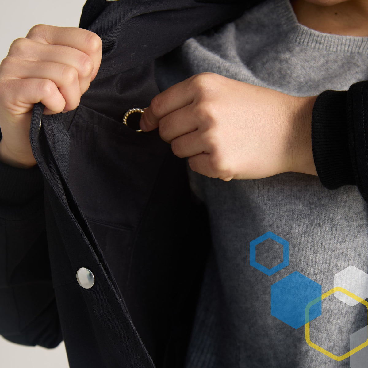 women's black curie lab coat with small hidden jewelry or valuables pocket inside the upper breast pocket. Girl is placing a gold ring inside for safe keeping.
